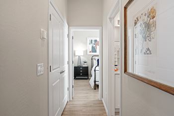 A hallway with white walls and white doors and a white bedroom with a white bed